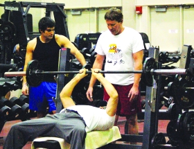 Sinclair students Zach Vanzant (on left) and Jeff Benfield (on right) spot instructor John McDaniel on the bench press in the weight room. The weight room is located in Bldg. 8 Room 112. --photo by Mary Edwards